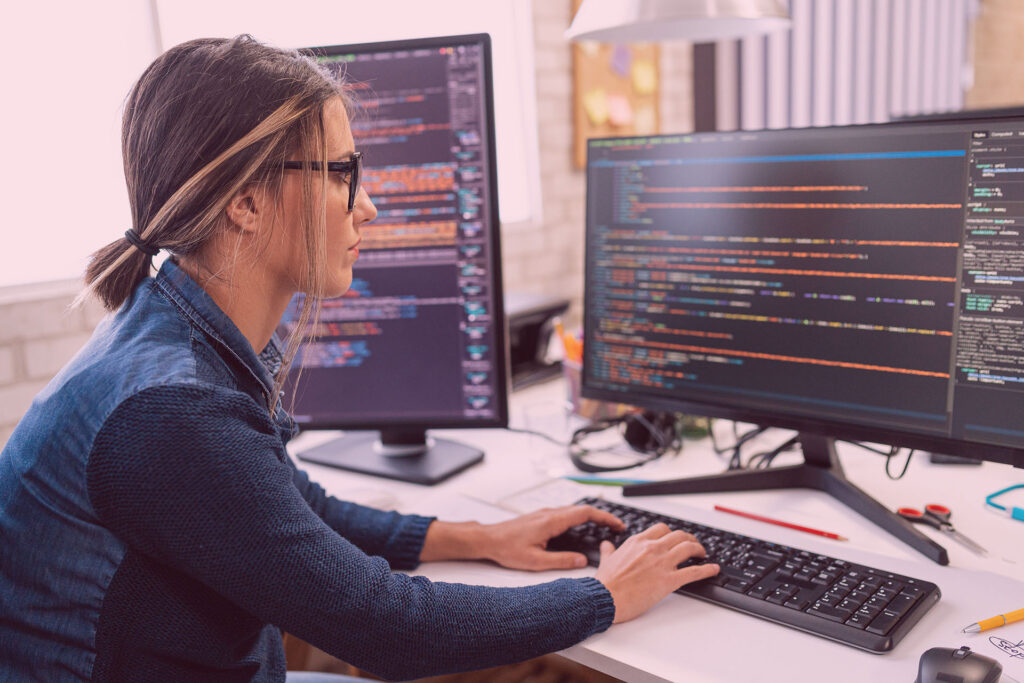 Woman sitting at a desk coding on a computer with two monitors